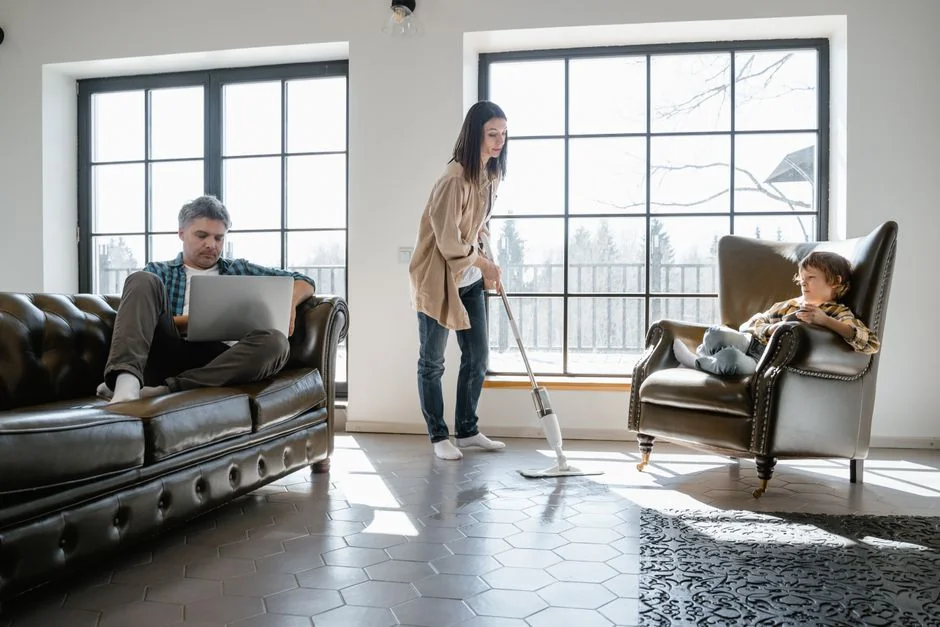 A woman in a gray sweater wipes a table with care, showcasing home cleaning in comfort.
