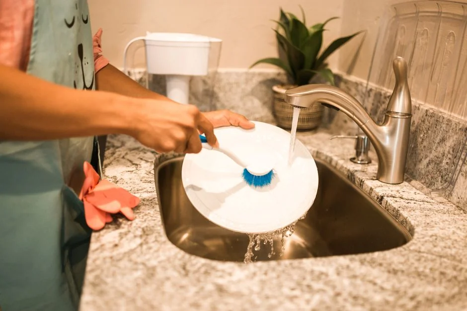 Profile view of a young concentrated woman in latex gloves standing in a bright room during the day while cleaning a mirror